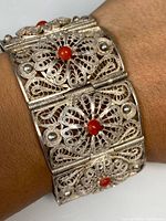 Close-up view of the front side of the silver filigree bracelet showing central coral inset stones on floral panels.