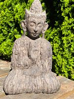 Front view of an Asian Buddha statue showing detailed facial features, seated posture, and textured surface.
