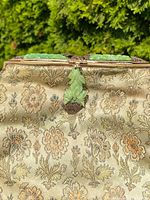 Close-up of the top clasp area showing carved green jade inset set in an ornate silver gilt frame with silk embroidered floral fabric beneath.