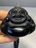 Front view of carved black onyx Buddha pendant held by hand showing detailed carving and glossy finish.