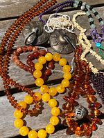 Photo showing collection of various beaded jewelry including bracelets and necklaces in amber, yellow, red, purple, green, and cream colors along with two metal finger cymbals.