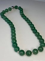 Full view of the jade beaded necklace laid flat, showing the spherical jade beads and the silver clasp.