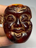 Front view of carved amber Buddha head bead showing smiling face and detailed hair carving.