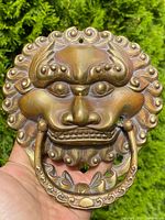 Single bronze foo lion door knocker held in hand against greenery