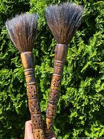 Pair of antique paint brushes with carved wooden handles and full horse hair bristles held outdoors.