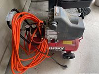 Full side view of the Husky air compressor with attached orange air hose coiled on the side.