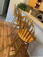 Photo showing three wooden swiveling barstools lined up side by side with visible spindle backs and natural wood finish.