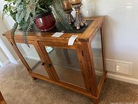 Front and side angle showing wood frame, glass doors, shelves inside, and items on top which are not included.