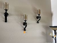 Three metal candle sconces with clear glass holders mounted on wall showing curved black metal supports.