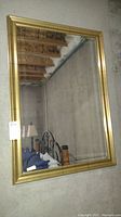 Full view of the large rectangular gold-toned framed beveled glass mirror leaning against a concrete wall.