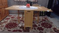 Front view of rectangular drop leaf dining table with cabinet under table and wooden chairs stored inside.
