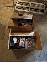 Two open boxes with DVDs and CDs inside, visible titles including 'Weeds' and various DVDs stacked horizontally and vertically.