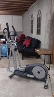 Side view of CardioMax elliptical machine set in a basement room with concrete walls and carpeted flooring.