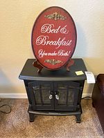 Front view of black plastic lighted fireplace heater with glass inset doors and sides, and red Bed & Breakfast sign on wooden stand atop heater.