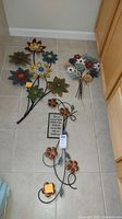 Three pieces of floral metal wall art arranged on floor, showing variety of flower sizes and colors