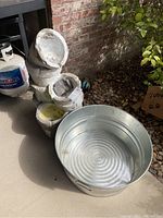 Photo showing the stacked concrete fountain shell and galvanized washtub next to a wall outdoors.