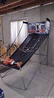Full view of the collapsible free throw basketball game showing the black ramp with basketball court markings, two orange hoops with nets, metal frame, and four basketballs on the lower ramp.