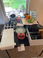 View of tabletop with kitchen items including glass storage, electric griddle, miscellaneous kitchenware, ceramic pieces, Insignia CD radio, and various kitchen tools