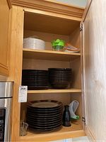 Three cabinet shelves holding Mikasa brown plates and bowls, paper plates, hand chopper, and kitchen accessories
