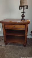 Full view of one nightstand with drawer closed and a lamp on top.