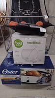 Oster 20-quart roaster oven box, Food Network punch bowl set box, and black plastic party flutes stacked for display.