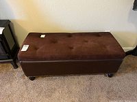 Full view of brown padded storage bench with tufted lid and leather base, showing overall shape and design.