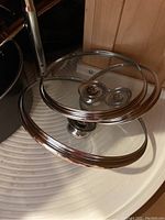 Three glass pot lids stacked, showing metal rims and handles.