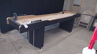 Full view of black shuffleboard table with metal legs and scoring rack