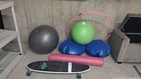 Photo of exercise equipment and skateboard including two exercise balls, yoga mat, yoga blocks, light-up hula hoop, and Dusters longboard skateboard on floor.