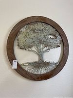 Full view of wood framed metal tree wall art hung on wall, showing circular design and tree sculpture inside.