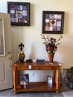 Photo of the wooden table with tall vase with faux flowers, gold-toned decorative object, 'Mr.' and 'Mrs.' signs, and two framed wall art pieces hung above.