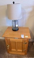 Full view of the wooden side table with a lamp placed on top, showing the light oak finish and brass hardware.