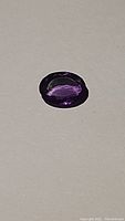 Oval cut deep purple amethyst gemstone on light background showing color and clarity