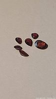 Six natural cherry red garnet gemstones in various shapes and cuts laid out on a neutral surface, showing color and clarity.