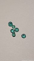 Six round cut natural emeralds on a neutral background showing size, shape and color.