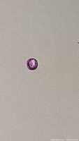 Close-up photo of the oval cut purple-pink sapphire on a plain background showing clarity and color
