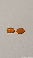 Two oval cabochon cut Ethiopian fire opals in bright Fanta orange color showing characteristic opal flashes.