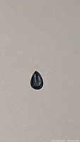 Top-down view of natural blue sapphire pear cut gemstone on neutral background.