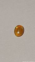 Photo of oval cabochon cut chocolate opal displaying warm brown base color and bright orange and green flash.