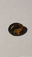 Oval faceted deep cognac colored Madeira citrine gemstone placed on a white background, showing the stone's color and facet pattern from top angle.
