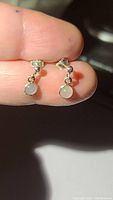 Photo showing front and side view of small natural moonstone earrings in sterling silver held between fingers