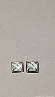 Two square cut aquamarine stones side by side on a light background showing one slightly larger than the other.