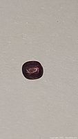 Photo of natural pink purple spinel gemstone, cushion cut shape lying on a light surface showing color and clarity.
