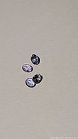 Four small natural tanzanite gemstones of varying color tones on neutral background