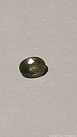 Oval cut natural olive green sapphire on a plain background showing color and facets.