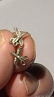 Close-up photo of one sterling silver hairdresser scissors stud earring held between fingers showing detailed design and post.
