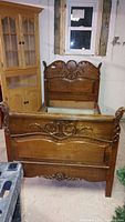 Full view of antique twin bed frame showing carved wood headboard and footboard in room with rustic walls and window.