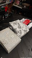 Three folded bedding sets arranged on a wooden surface showing different decorative patterns and packaging