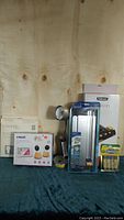 Full view of all items in the lot including baby monitor, head support, and craft supplies on green fabric background against wooden wall.