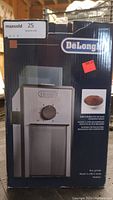 Front view of the DeLonghi burr coffee grinder in its box showing the brand and product image.